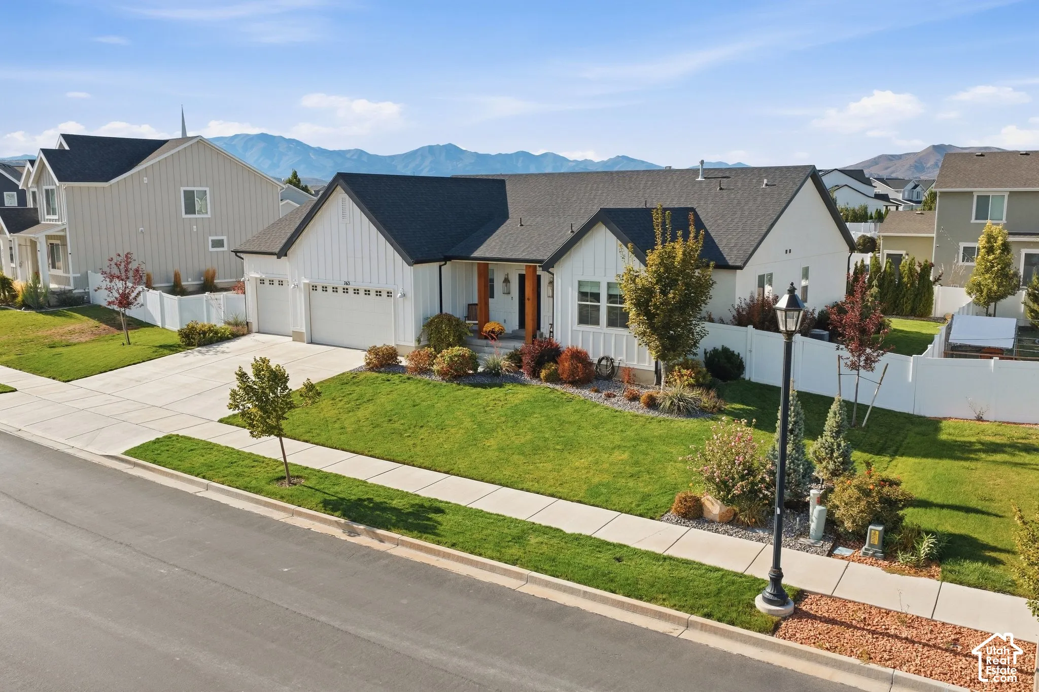 Modern farmhouse style exterior, two-car garage, concrete driveway, mature landscaping, and white privacy fence