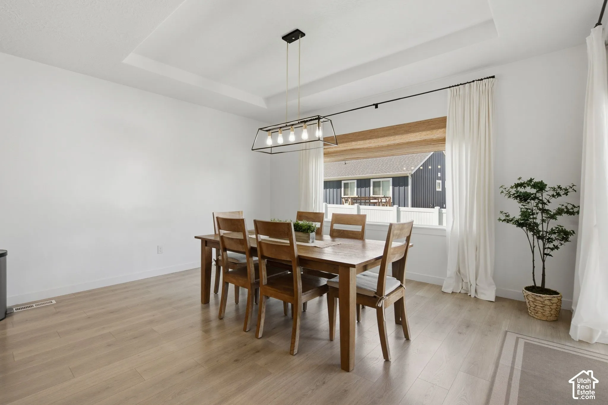 Tray ceiling accenting a contemporary linear chandelier, wide window, and wood-finish flooring