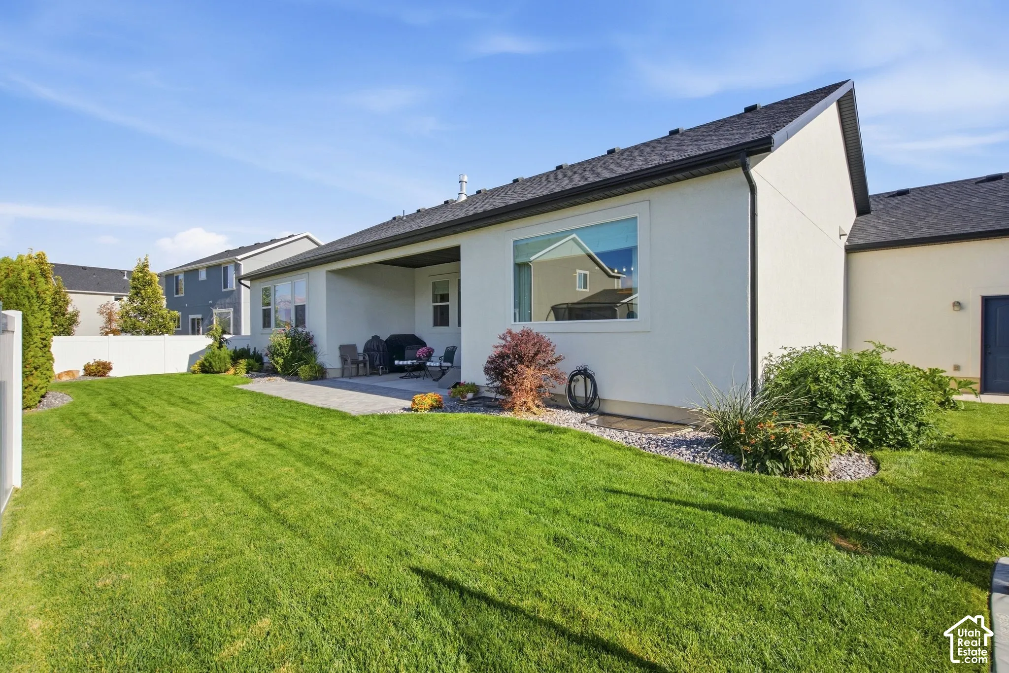 Expansive lawn area, covered patio, white vinyl fencing, and landscaped rock beds