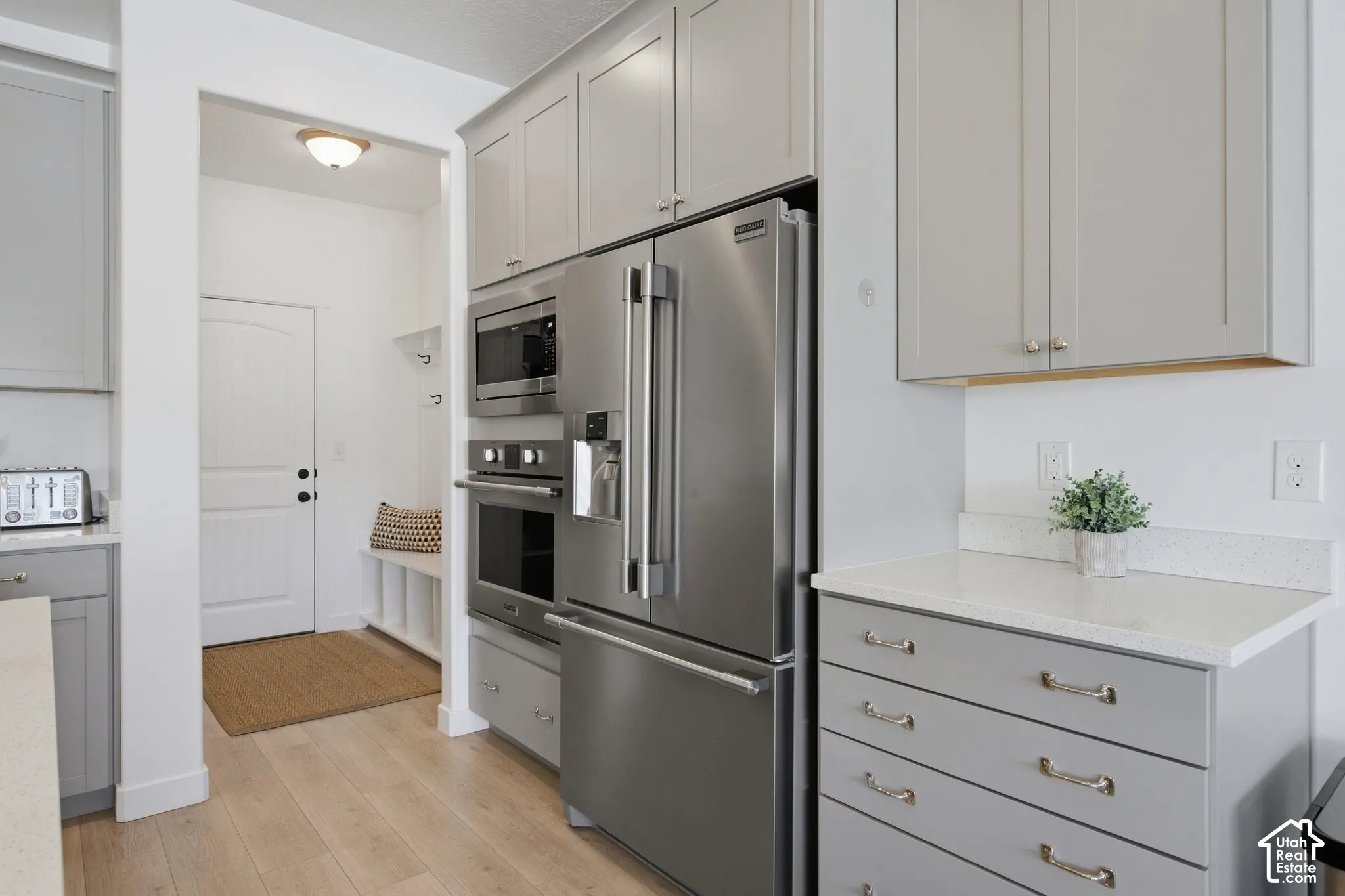 Stainless steel appliances, light wood-finish flooring, white countertops, and light gray cabinetry with brushed nickel hardware