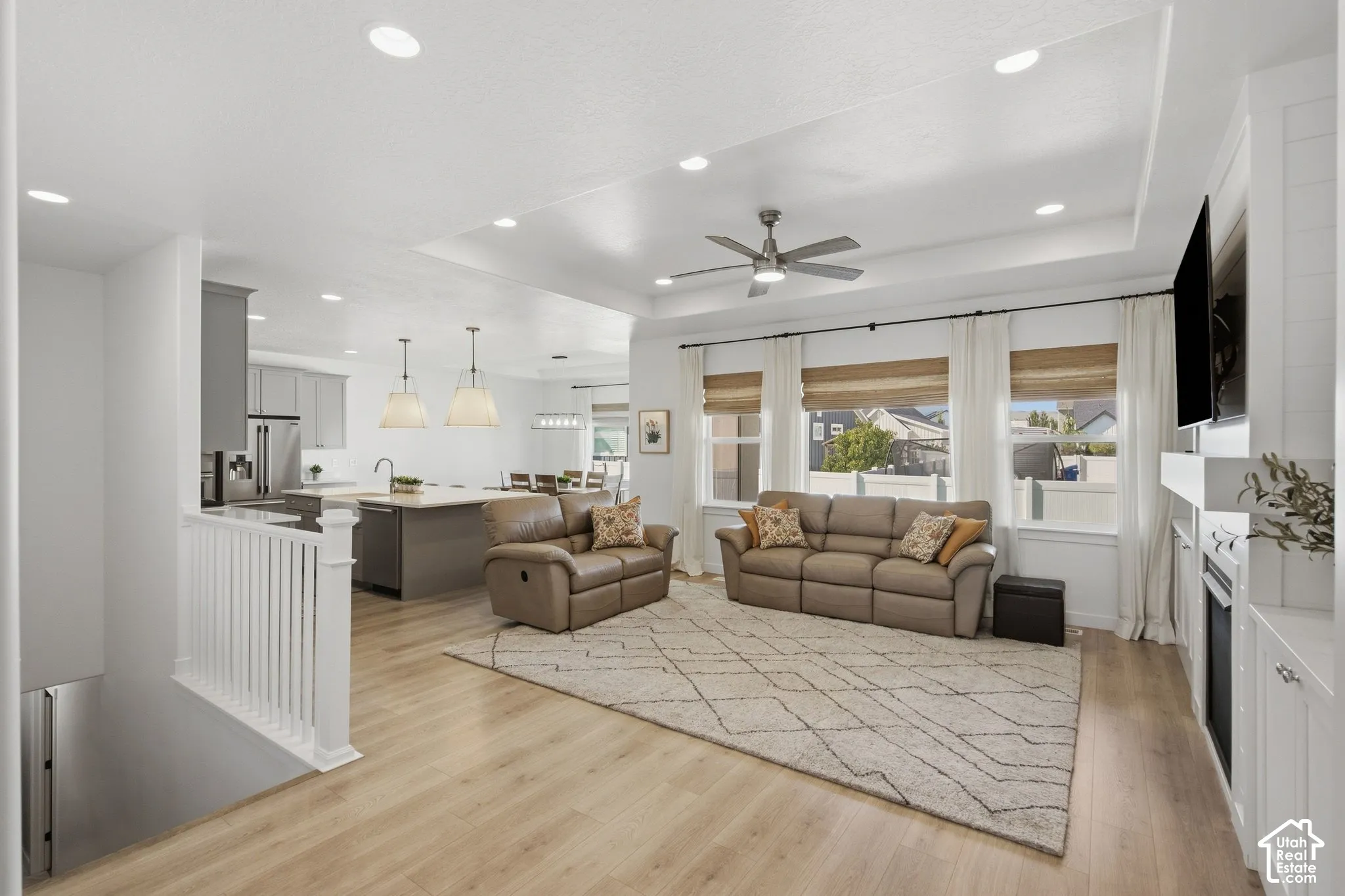 Open-concept living space featuring wood-finish flooring, a tray ceiling with a ceiling fan, and recessed lighting