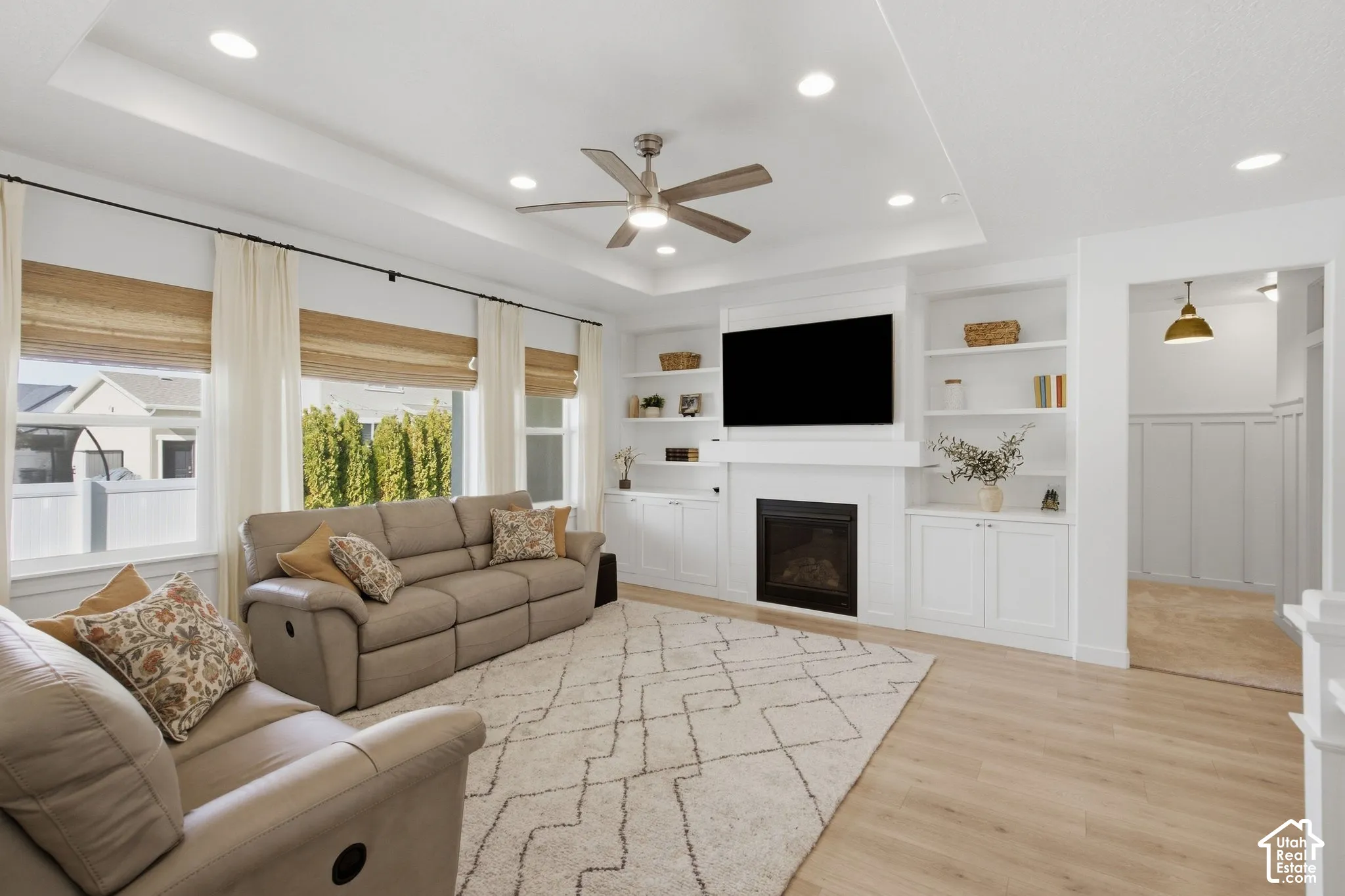 Recessed lighting throughout, tray ceiling with ceiling fan, built-in media center with fireplace, built-in shelving, and wood-finish flooring