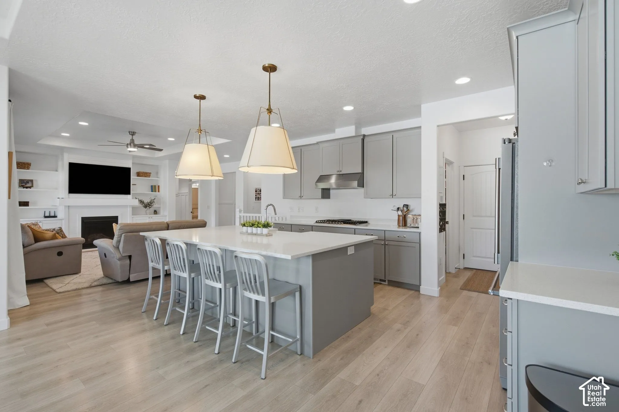 Light wood-finish flooring throughout, kitchen island with seating, recessed lighting, built-in shelving, and a fireplace with a hearth