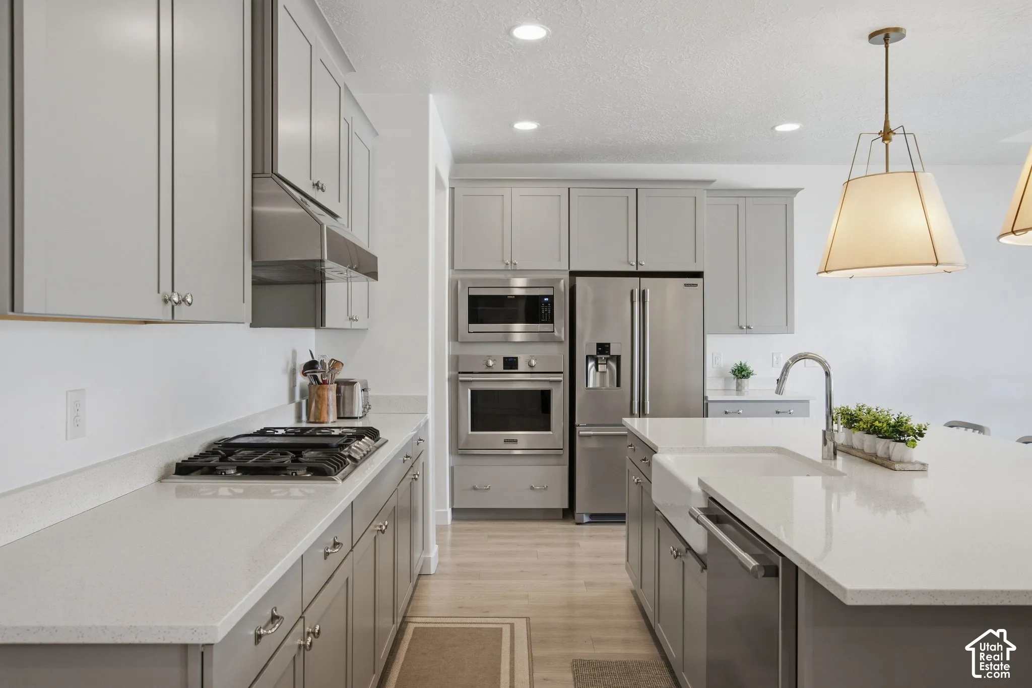 Kitchen featuring light gray cabinetry, stainless steel appliances, light-toned countertops, a built-in farmhouse sink, and pendant lighting