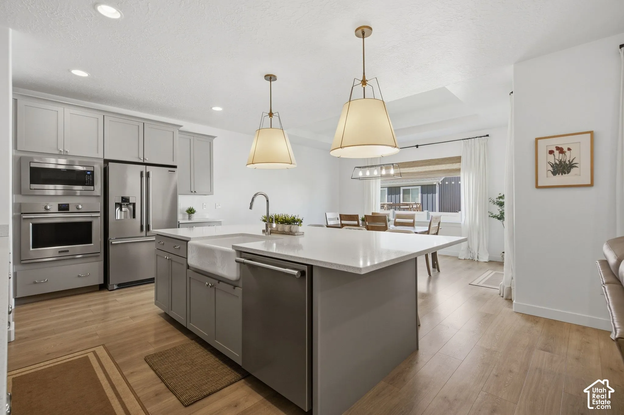 Kitchen featuring light gray cabinetry, stainless steel appliances, a center island with a farmhouse sink, and wood-finish flooring