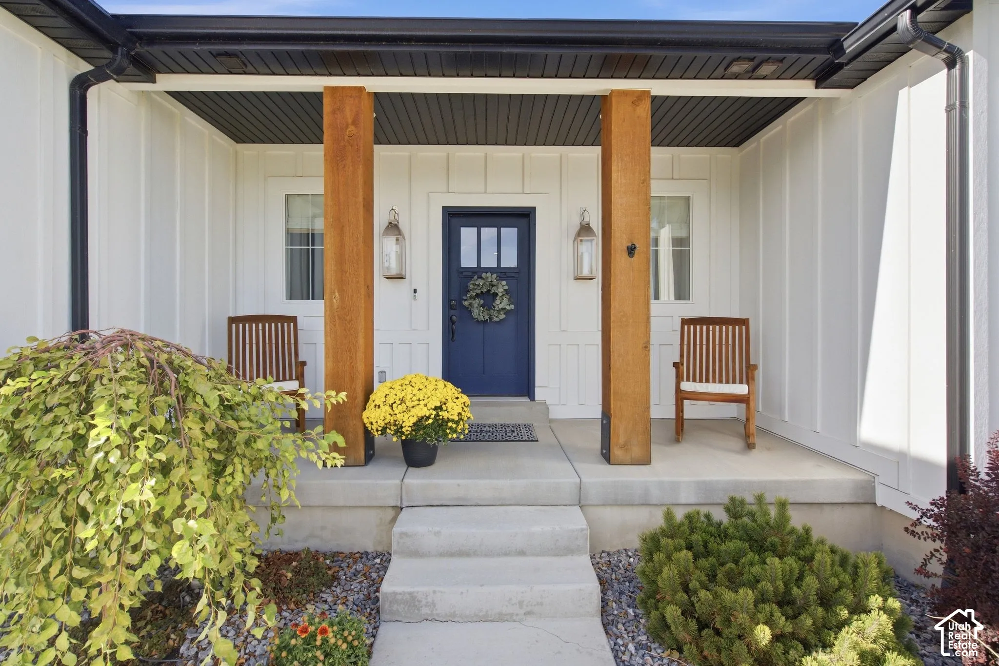 Board and batten siding with a covered concrete porch featuring wood posts, a dark blue entry door, and exterior sconces
