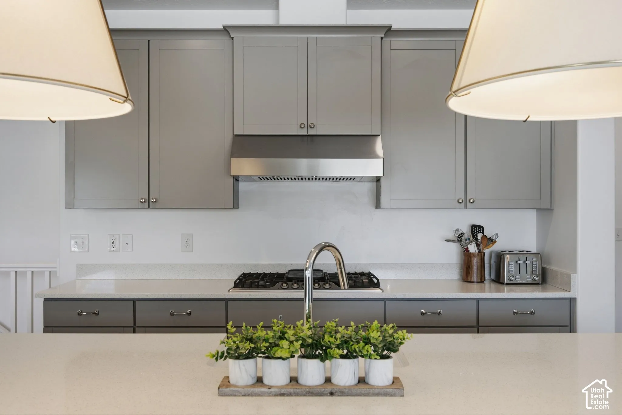 Gray cabinetry with stainless steel hardware, white countertops, stainless steel range hood, and a built-in gas cooktop