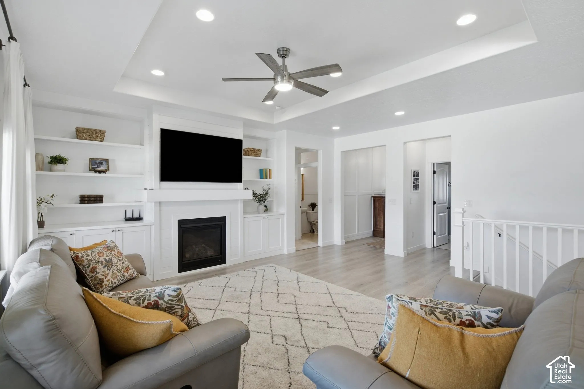 Living area featuring a tray ceiling, recessed lighting, ceiling fan, fireplace with mantel, and built-in shelving with cabinetry