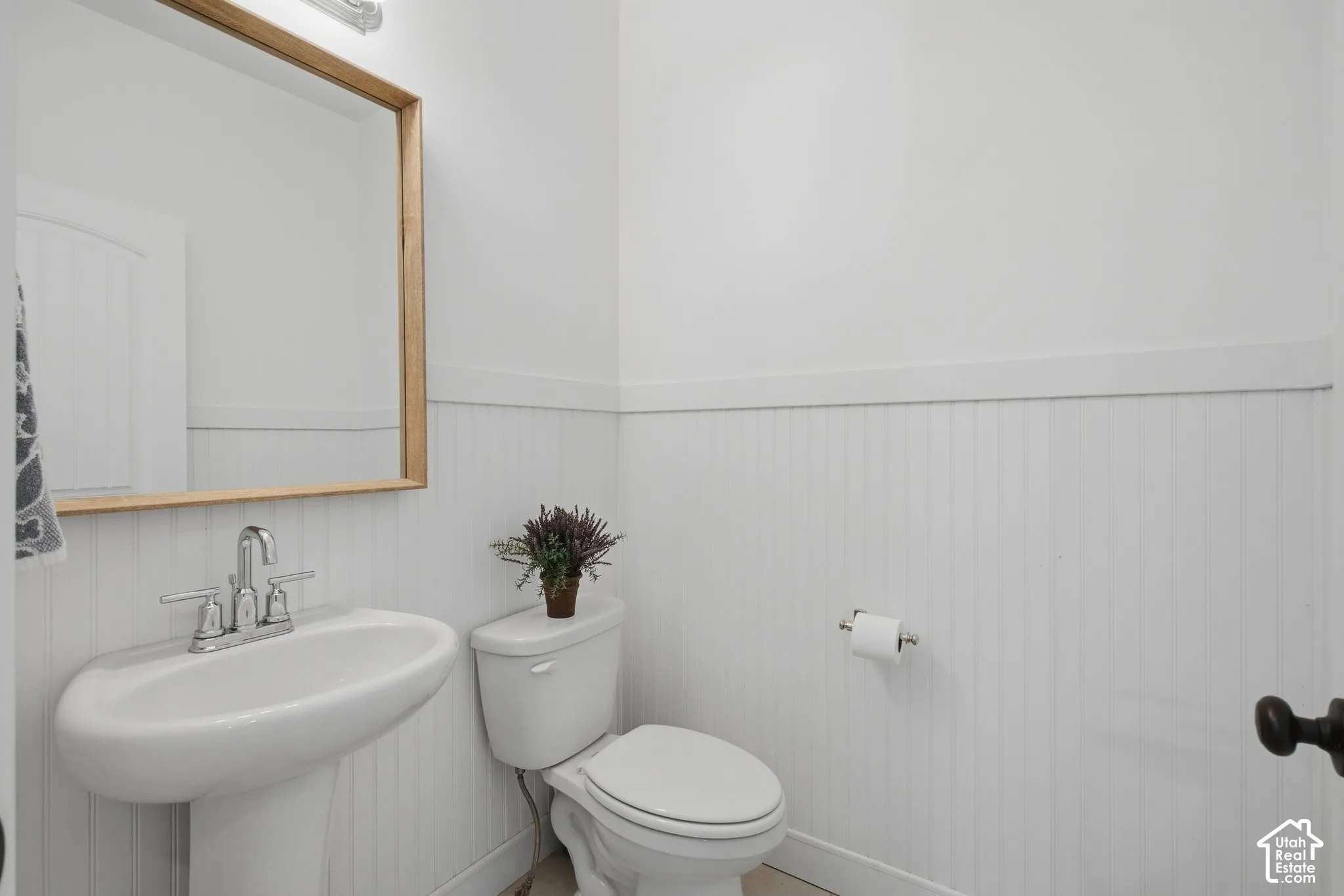 Pedestal sink with chrome faucet, wood-frame mirror, and white beadboard paneling