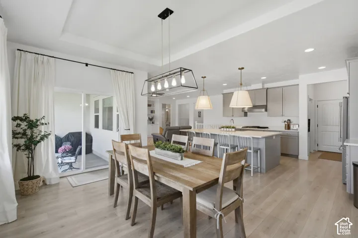 Tray ceiling with recessed lighting, light wood-finish flooring, white sliding glass doors, kitchen island with seating, and stainless steel appliances