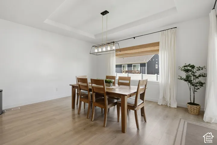 Tray ceiling accenting a contemporary linear chandelier, wide window, and wood-finish flooring