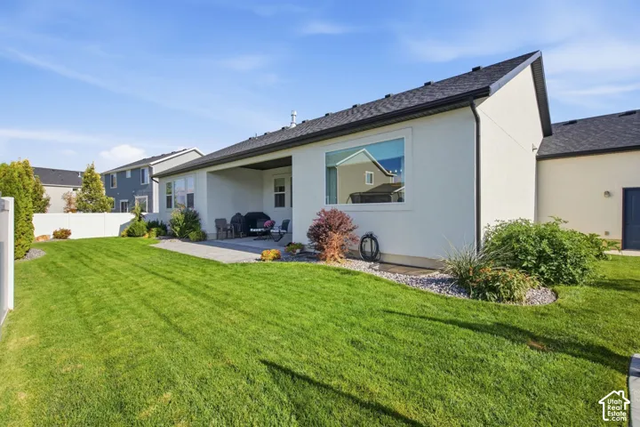Expansive lawn area, covered patio, white vinyl fencing, and landscaped rock beds