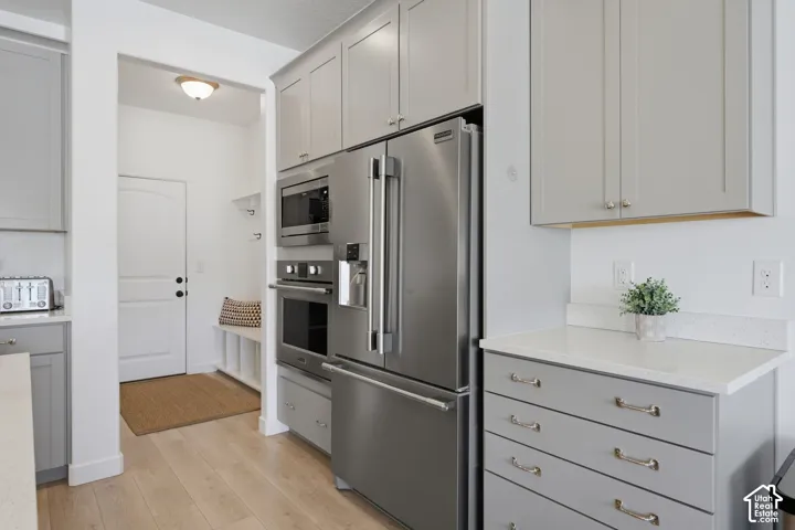 Stainless steel appliances, light wood-finish flooring, white countertops, and light gray cabinetry with brushed nickel hardware