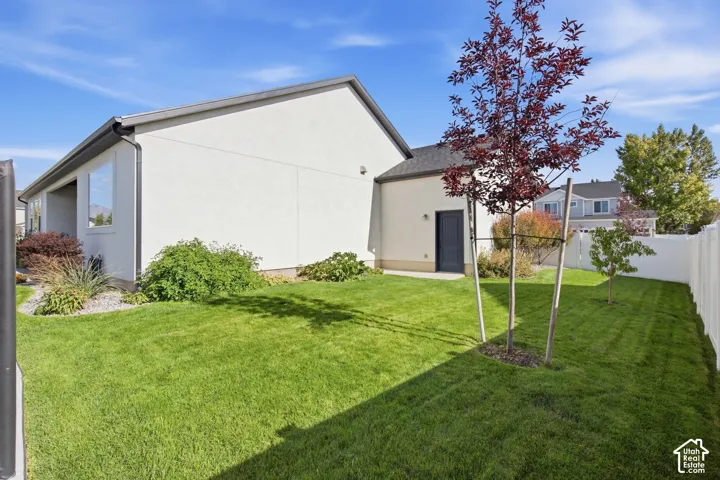Manicured lawn with a young deciduous tree, white vinyl fencing, and a stucco exterior