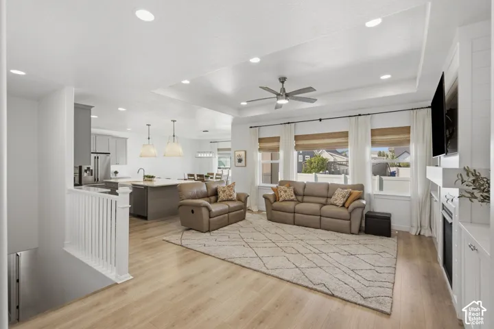 Open-concept living space featuring wood-finish flooring, a tray ceiling with a ceiling fan, and recessed lighting