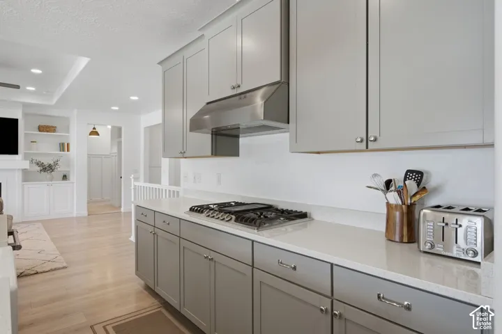 Light gray cabinetry with brushed nickel hardware, white countertops, and a stainless steel gas range with coordinating hood