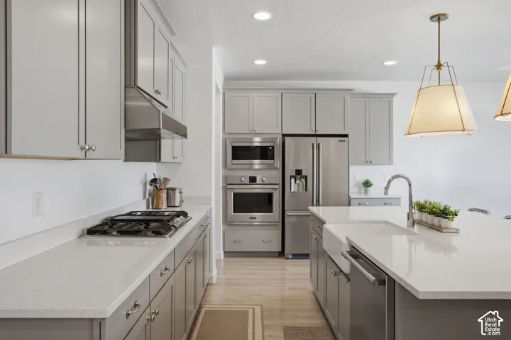 Kitchen featuring light gray cabinetry, stainless steel appliances, light-toned countertops, a built-in farmhouse sink, and pendant lighting