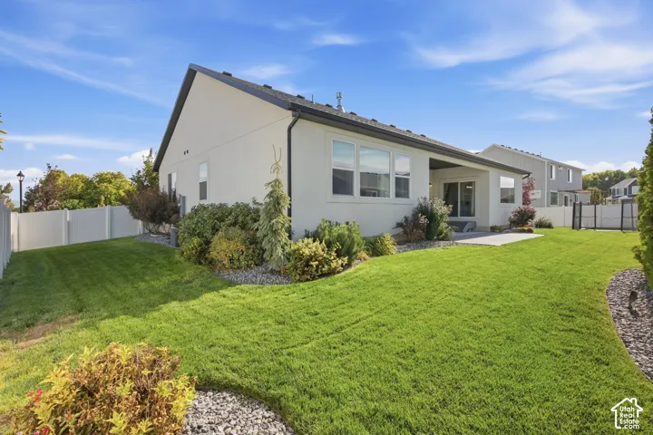 Exterior with light-colored siding, covered patio, multiple windows, and a landscaped yard featuring a white privacy fence