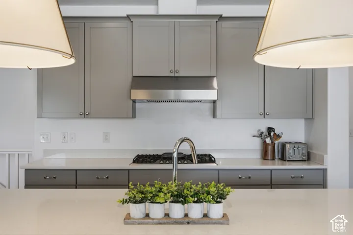 Gray cabinetry with stainless steel hardware, white countertops, stainless steel range hood, and a built-in gas cooktop