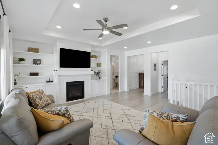 Living area featuring a tray ceiling, recessed lighting, ceiling fan, fireplace with mantel, and built-in shelving with cabinetry