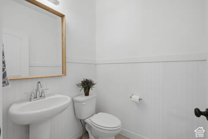 Pedestal sink with chrome faucet, wood-frame mirror, and white beadboard paneling