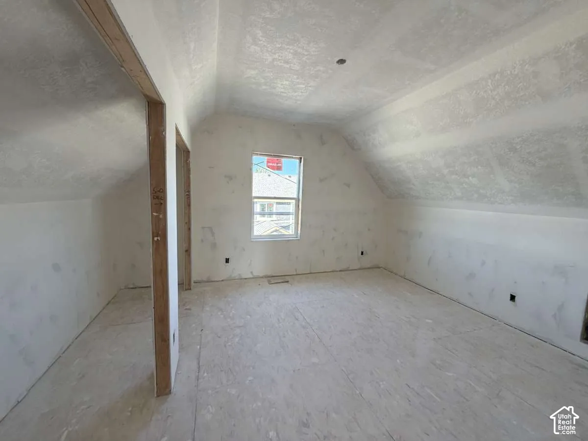 Unfinished room with sloped ceilings, plywood subflooring, and a single window