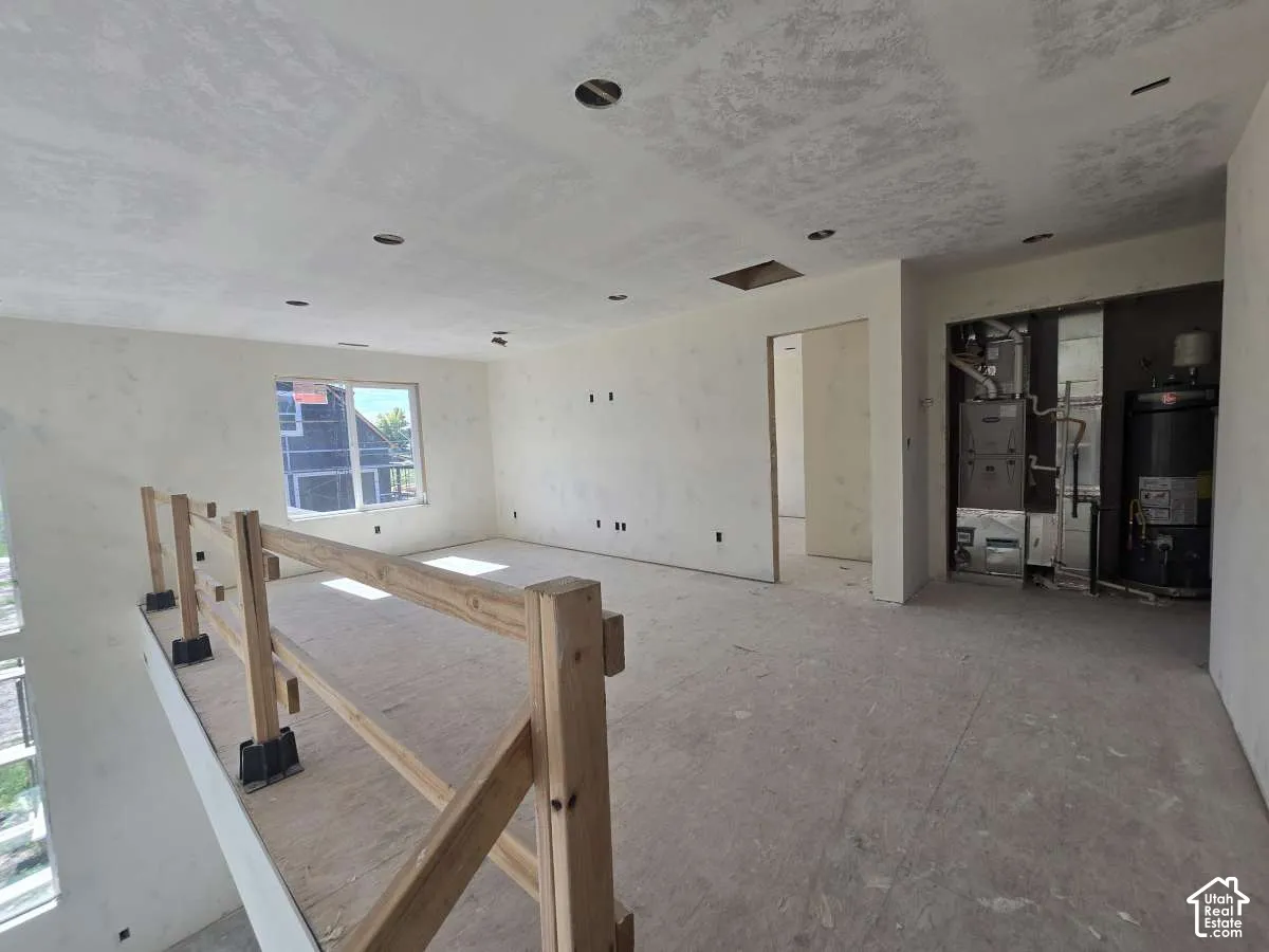 Open-concept interior featuring unfinished drywall, a large window, a partial wooden railing, and exposed utilities