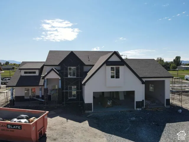 Two-story residence featuring a dark shingle roof, white stucco siding, dark brick facade accents, and an integrated garage structure