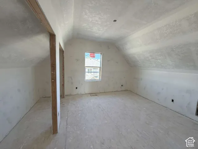 Unfinished room with sloped ceilings, plywood subflooring, and a single window