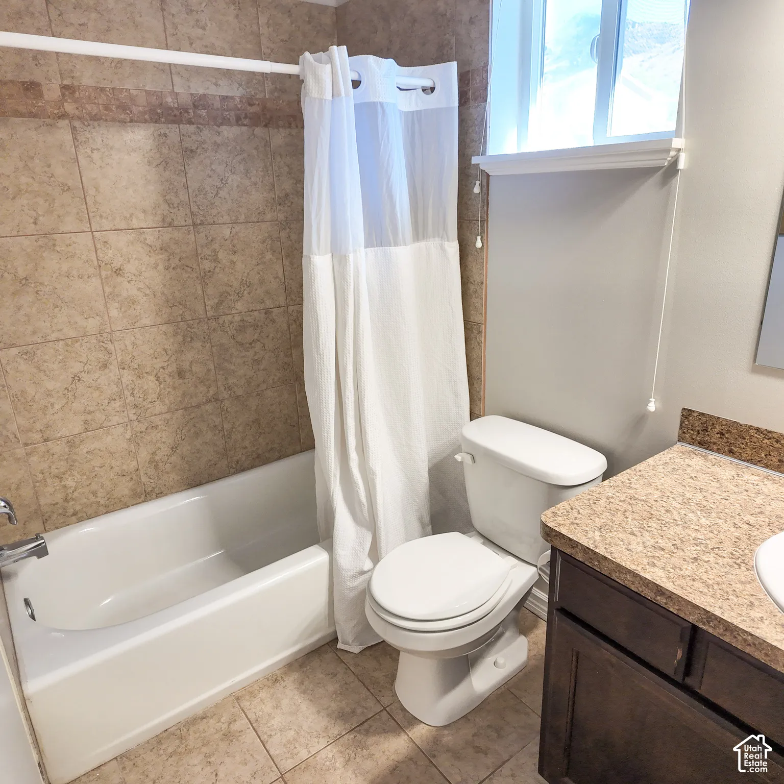 White bathtub with chrome fixtures, tiled shower surround, dual-flush toilet, and a vanity with a speckled countertop and dark wood-finish cabinetry