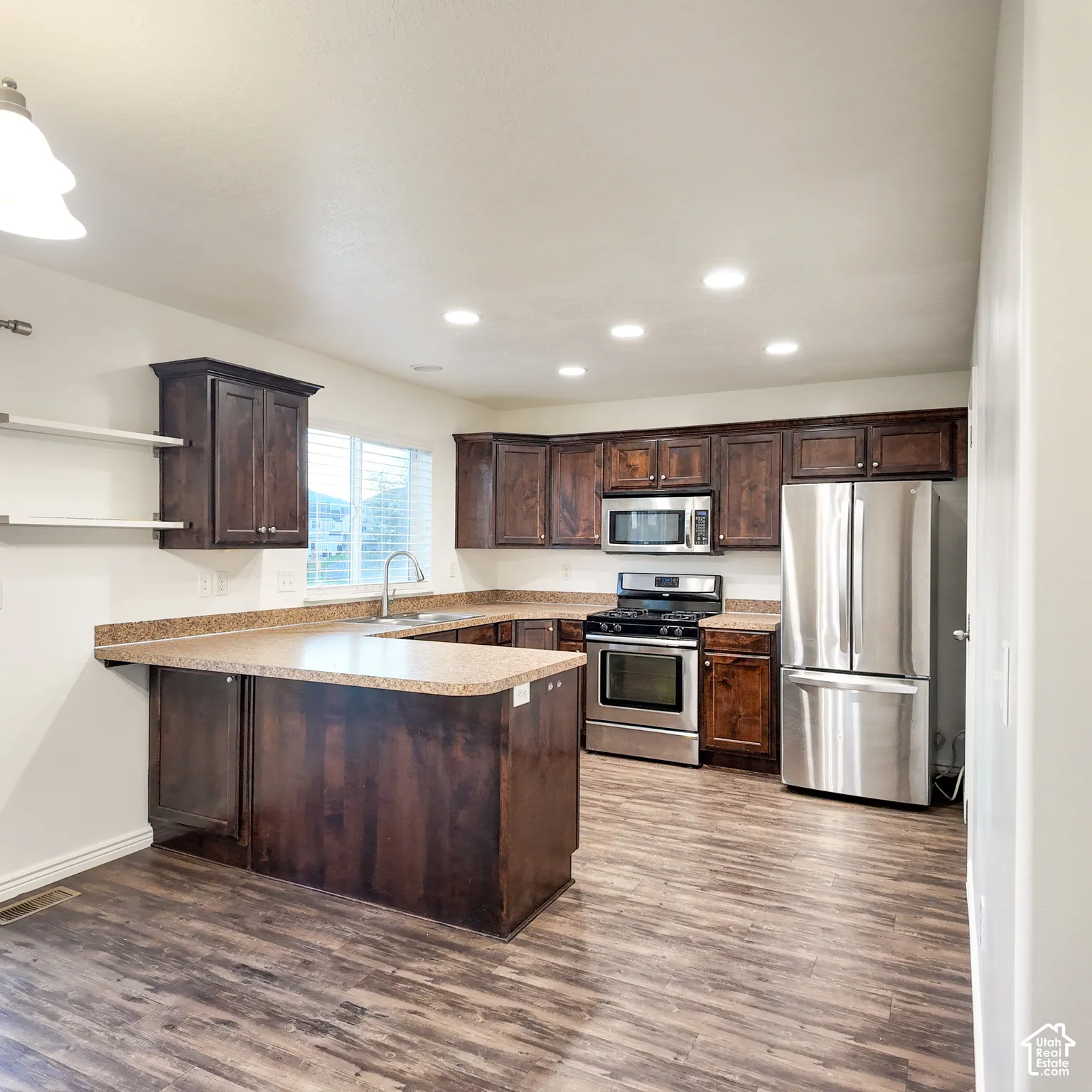 Wood-finish flooring, dark wood cabinetry, stainless steel appliances, recessed ceiling lighting, and a U-shaped countertop