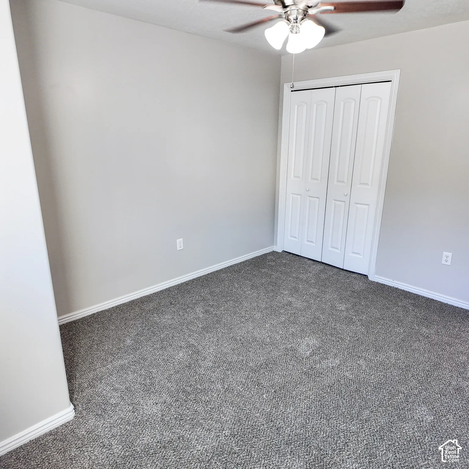 Neutral wall paint, gray carpeting, a ceiling fan with integrated lighting, and bi-fold closet doors
