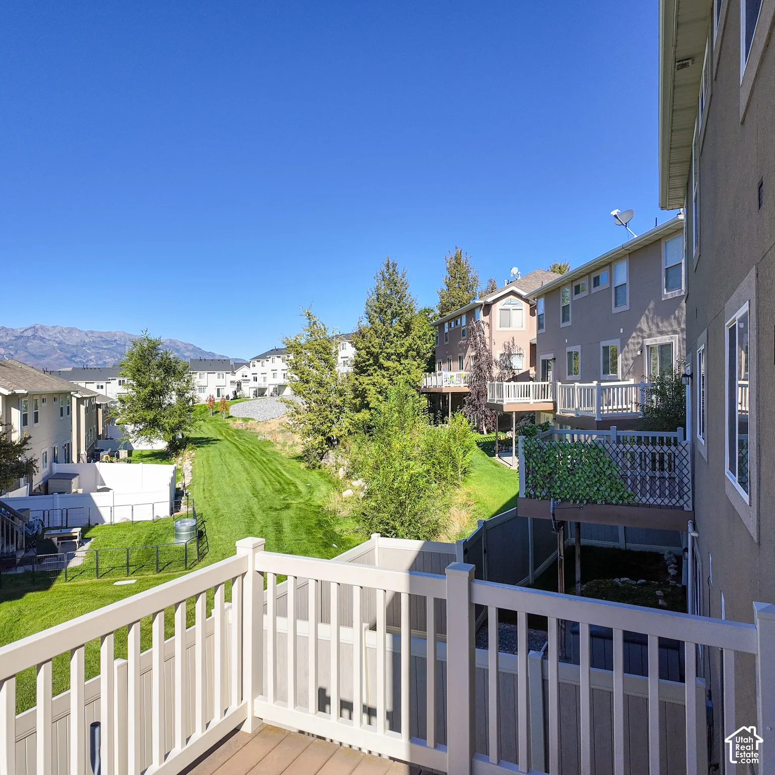 Wood-finish deck with white railing, overlooking a terraced backyard featuring a manicured lawn and mature landscaping