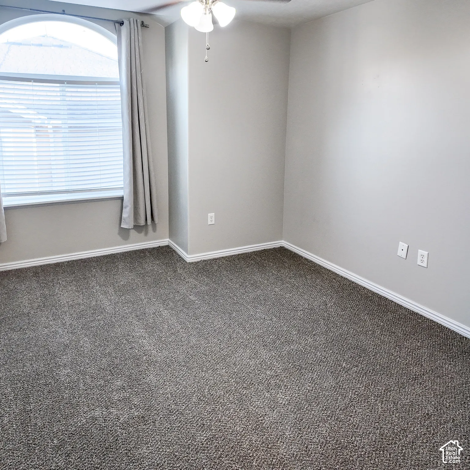 Arched window with blinds, ceiling fan with integrated lighting, and neutral wall paint