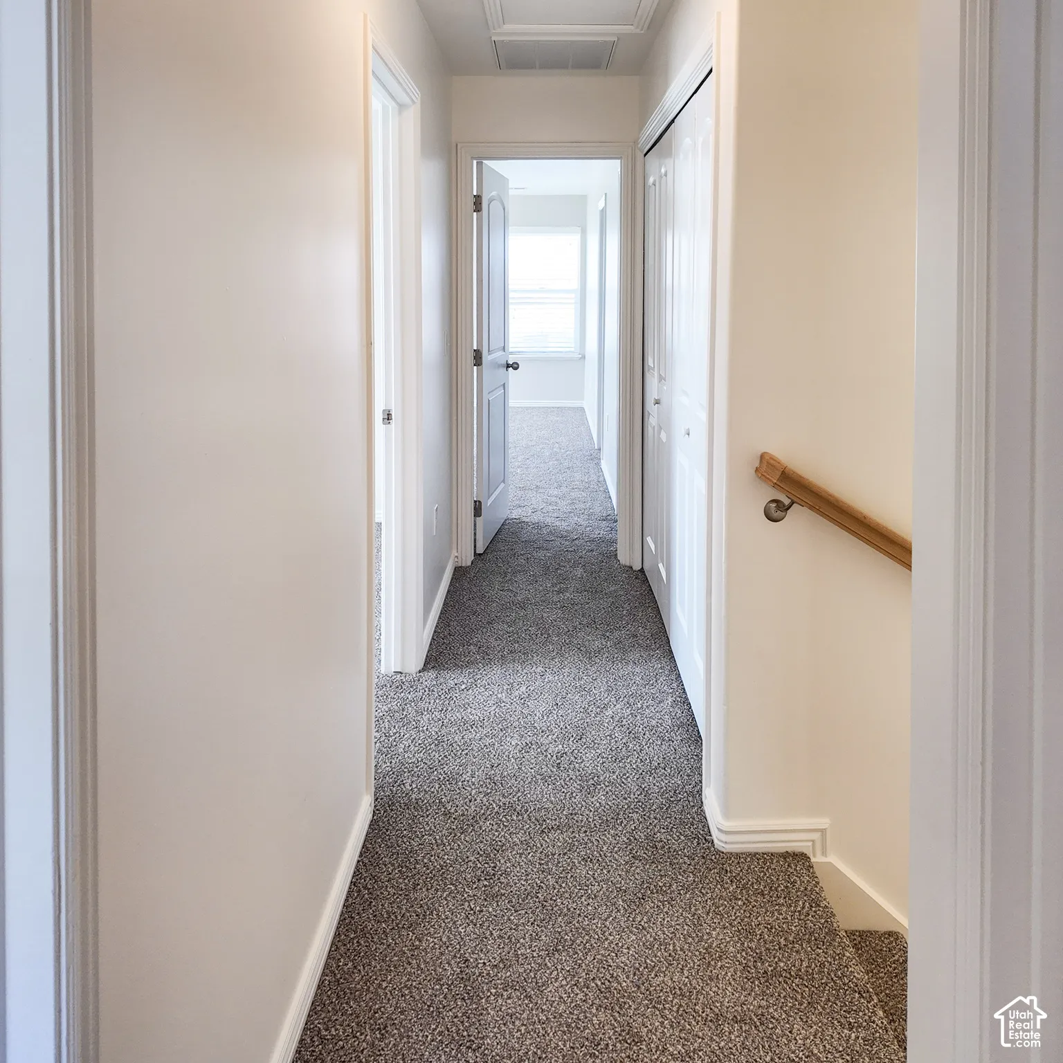 Neutral wall paint throughout, grey-toned carpeted flooring, white trim, and a natural wood handrail