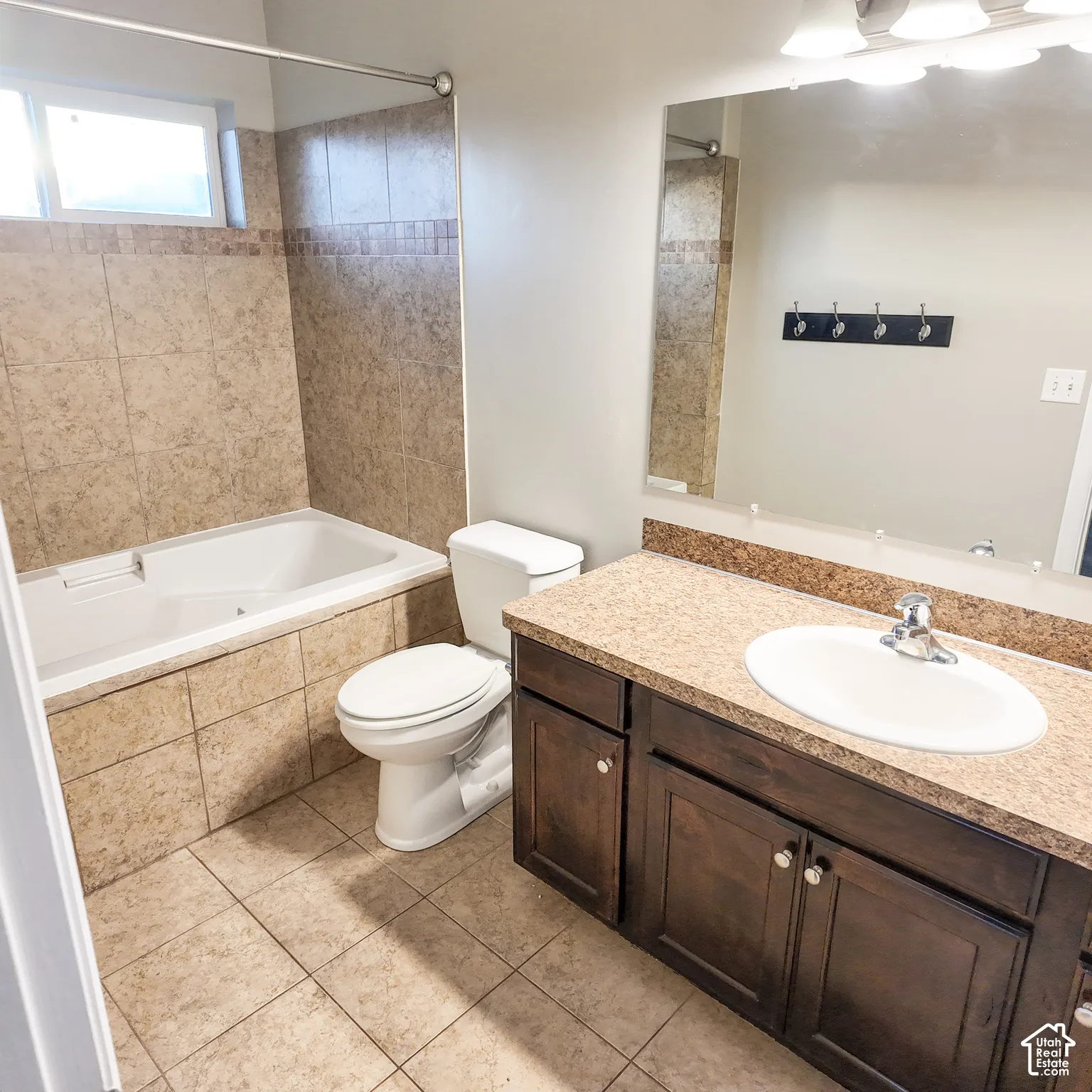Built-in bathtub with light-toned tile surround, single vanity with dark wood-finish cabinetry, speckled countertop, and large wall-mounted mirror