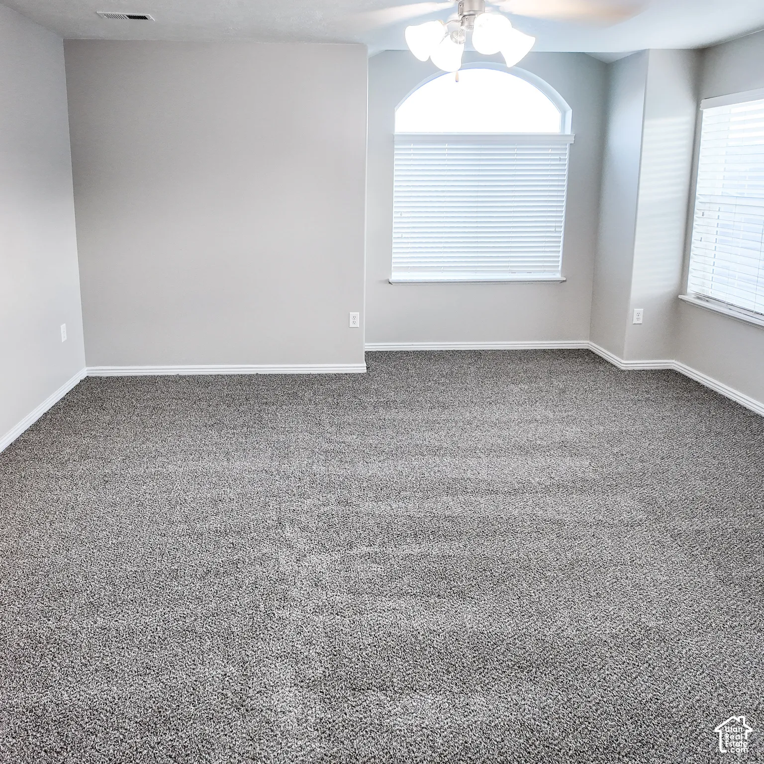 Carpeted room featuring a ceiling fan with integrated lighting, an arched window, and additional windows with blinds