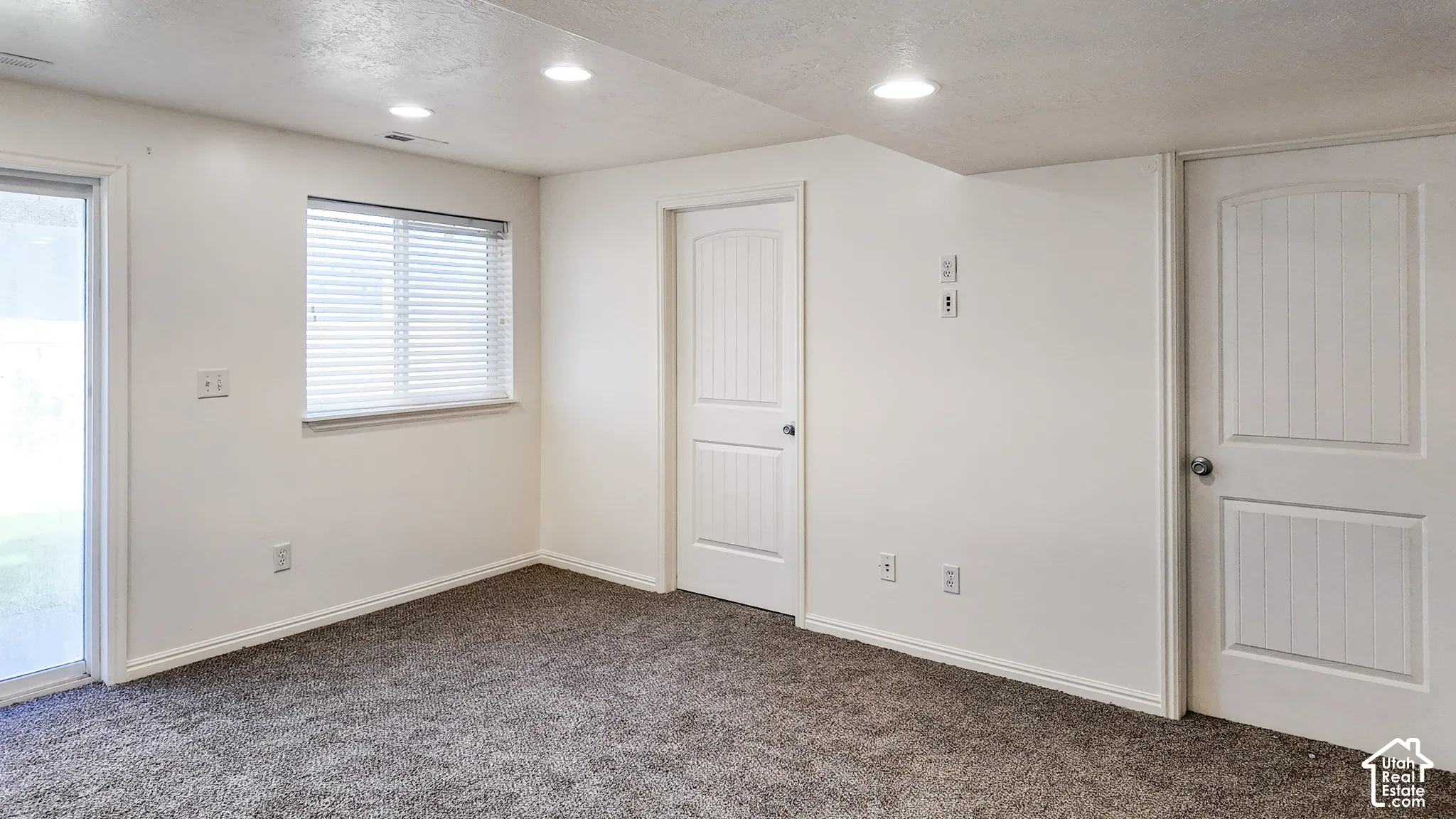 Recessed lighting, white walls, gray carpet flooring, white paneled doors, and a sliding glass door