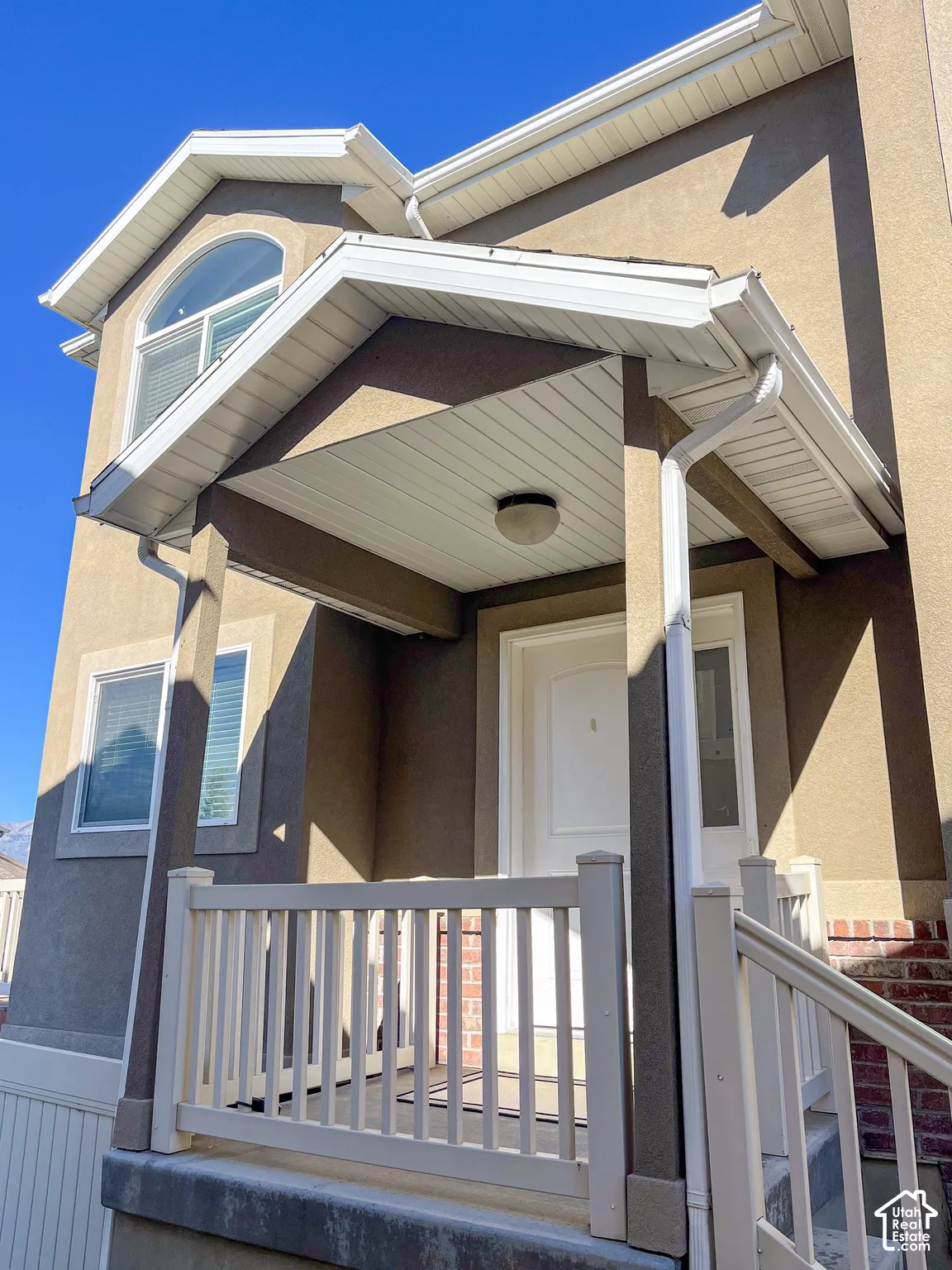 Covered entry with white porch railing, arched window, and stucco exterior