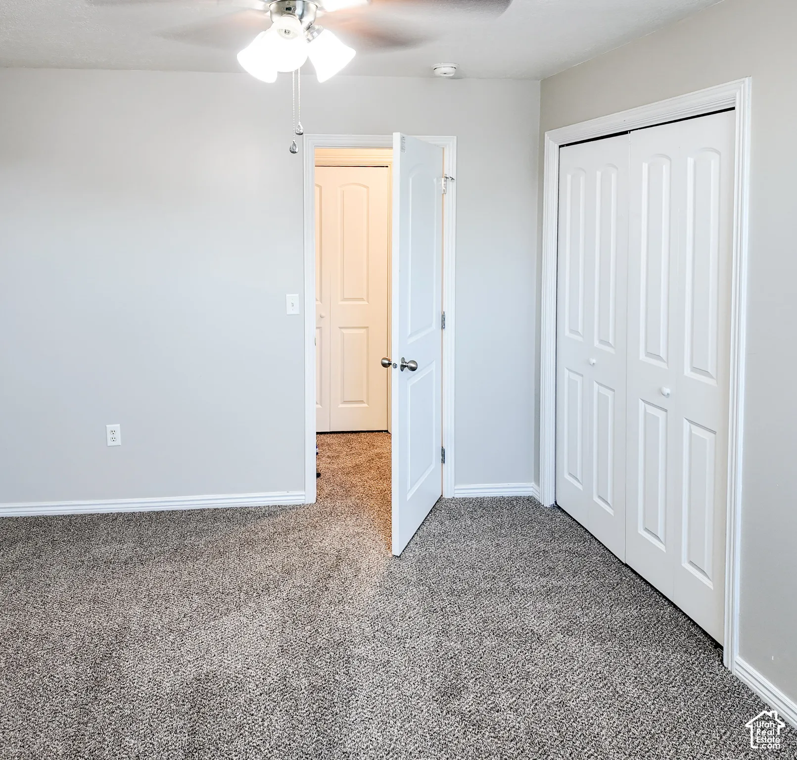 Neutral wall paint, textured carpet flooring, white trim, and a ceiling fan with integrated lighting