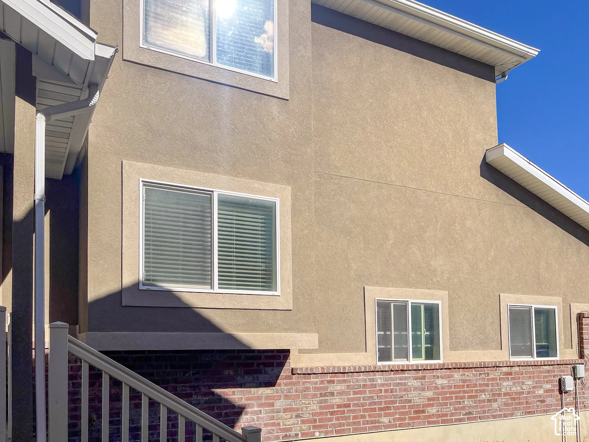 Stucco exterior with brick veneer accent, multiple windows, and white eaves