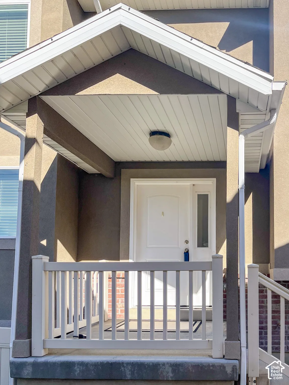 Covered porch entry featuring a white paneled door with glass insert, white railing, and an overhead light fixture