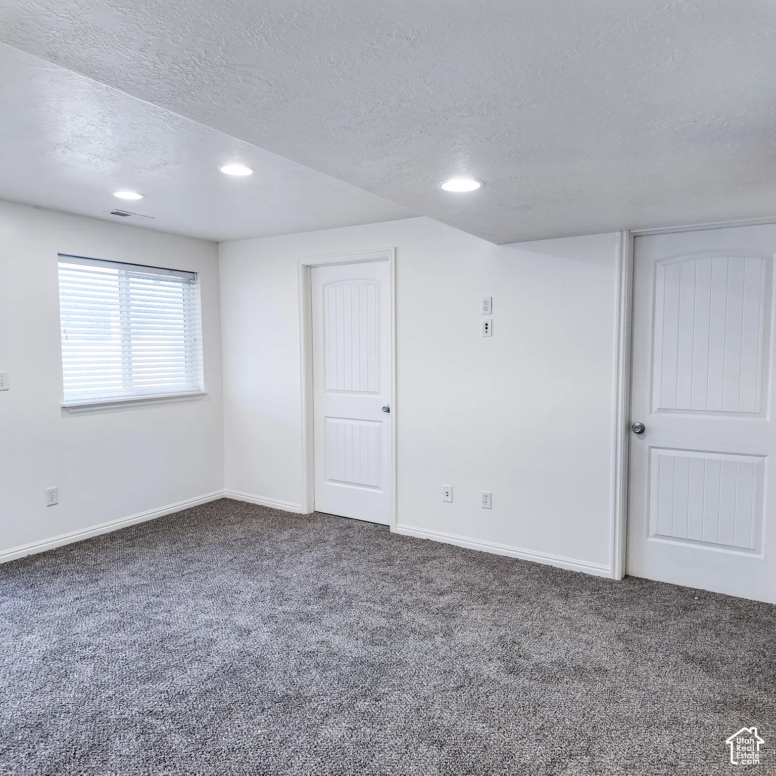 Recessed lighting, gray textured carpeting, white walls, white doors with panel detailing, and a window with blinds
