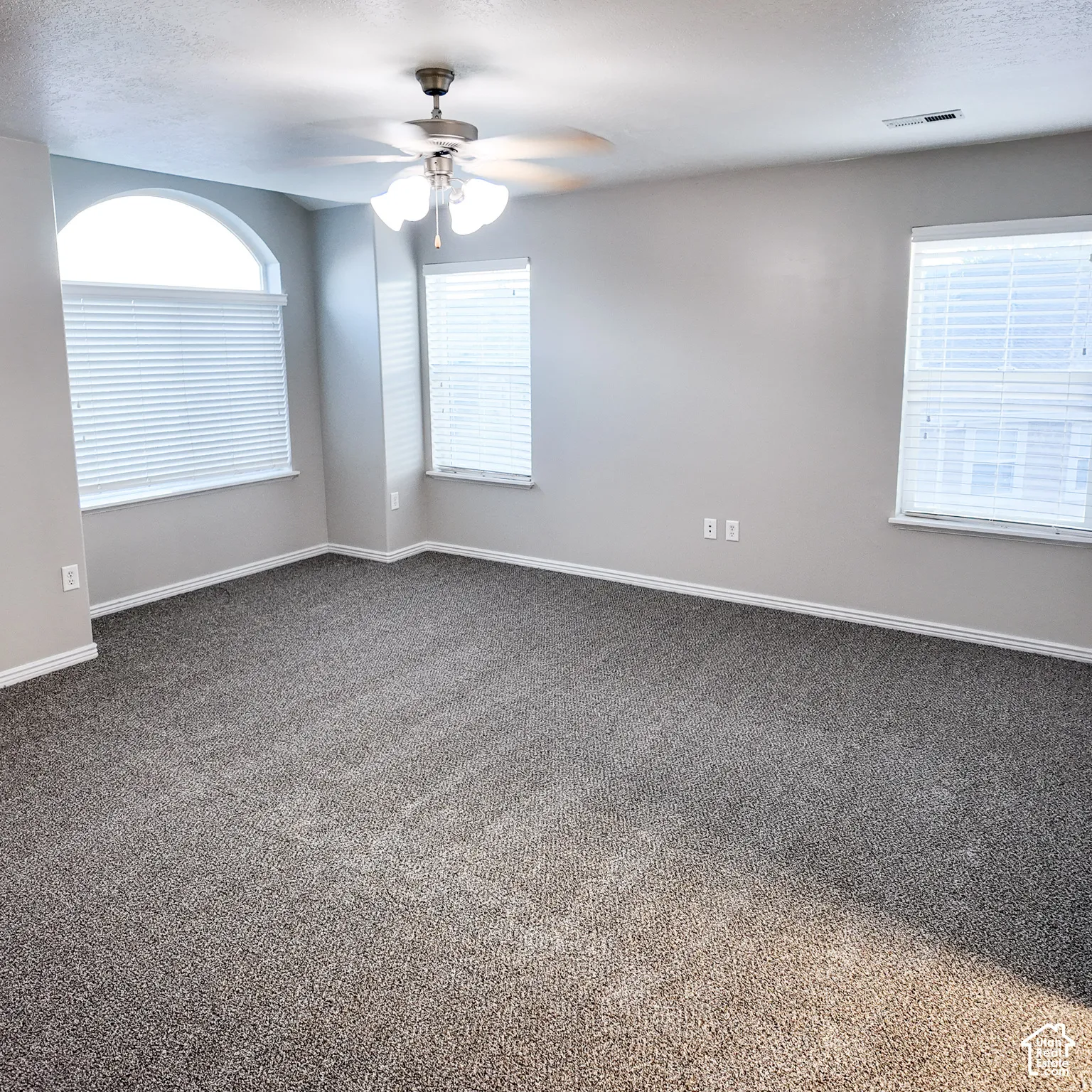 Arched window with two additional windows, ceiling fan, and grey carpet flooring