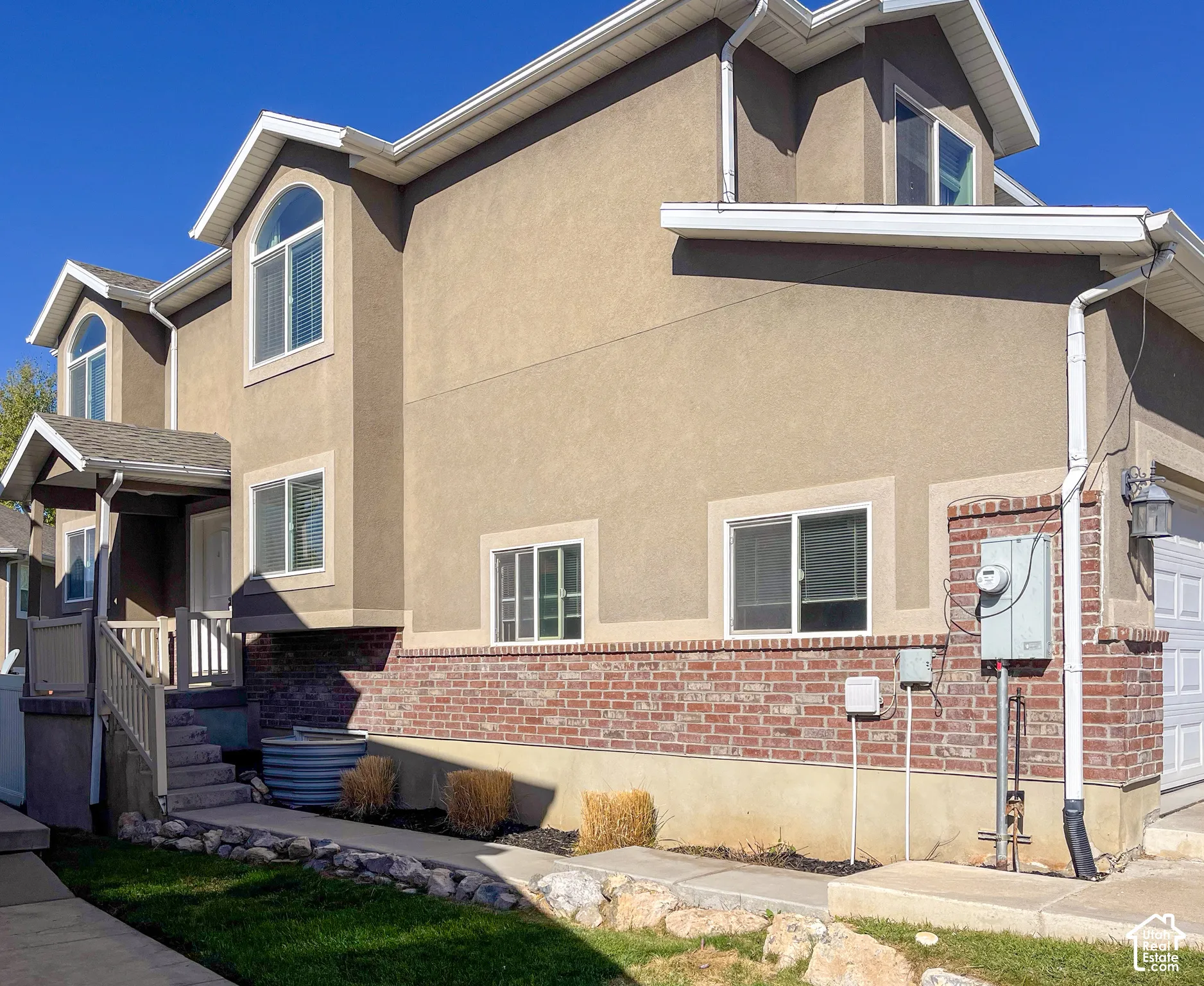 Stucco exterior with brick detailing, white window frames, and a covered entry