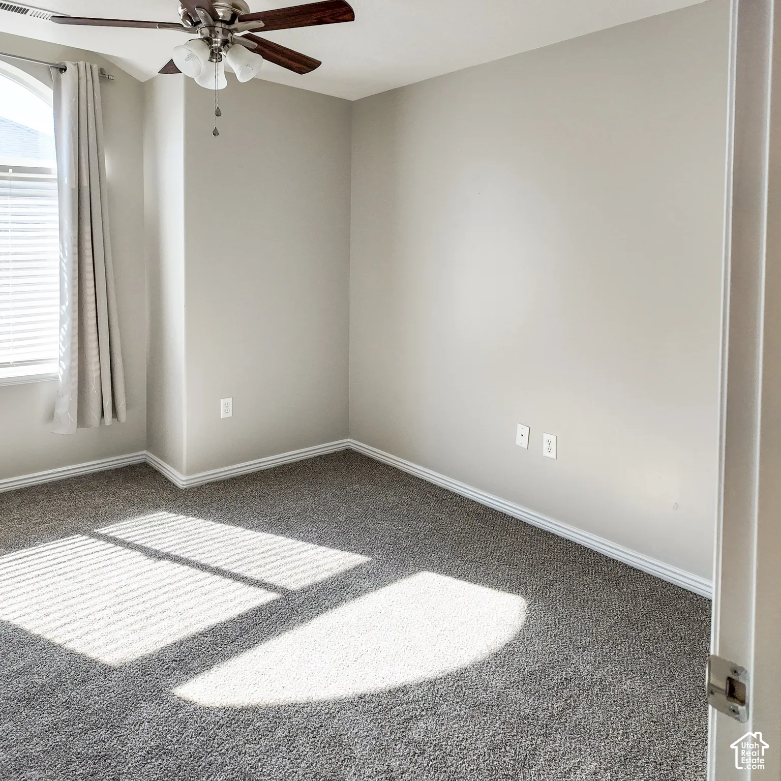 Neutral painted walls, gray carpet, and a ceiling fan with light fixture