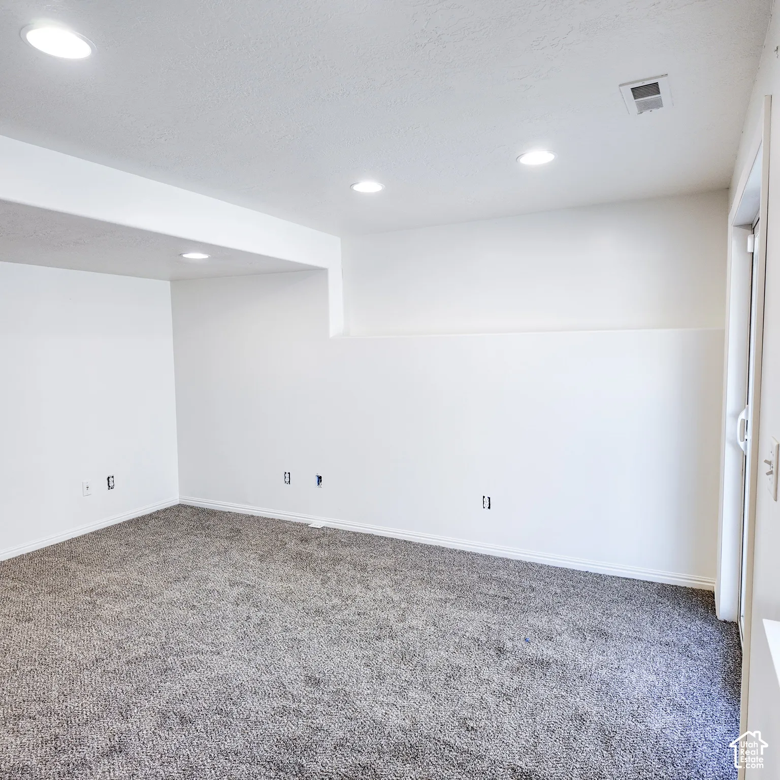 Recessed ceiling lighting, gray carpeting, neutral wall color, and a sliding glass door