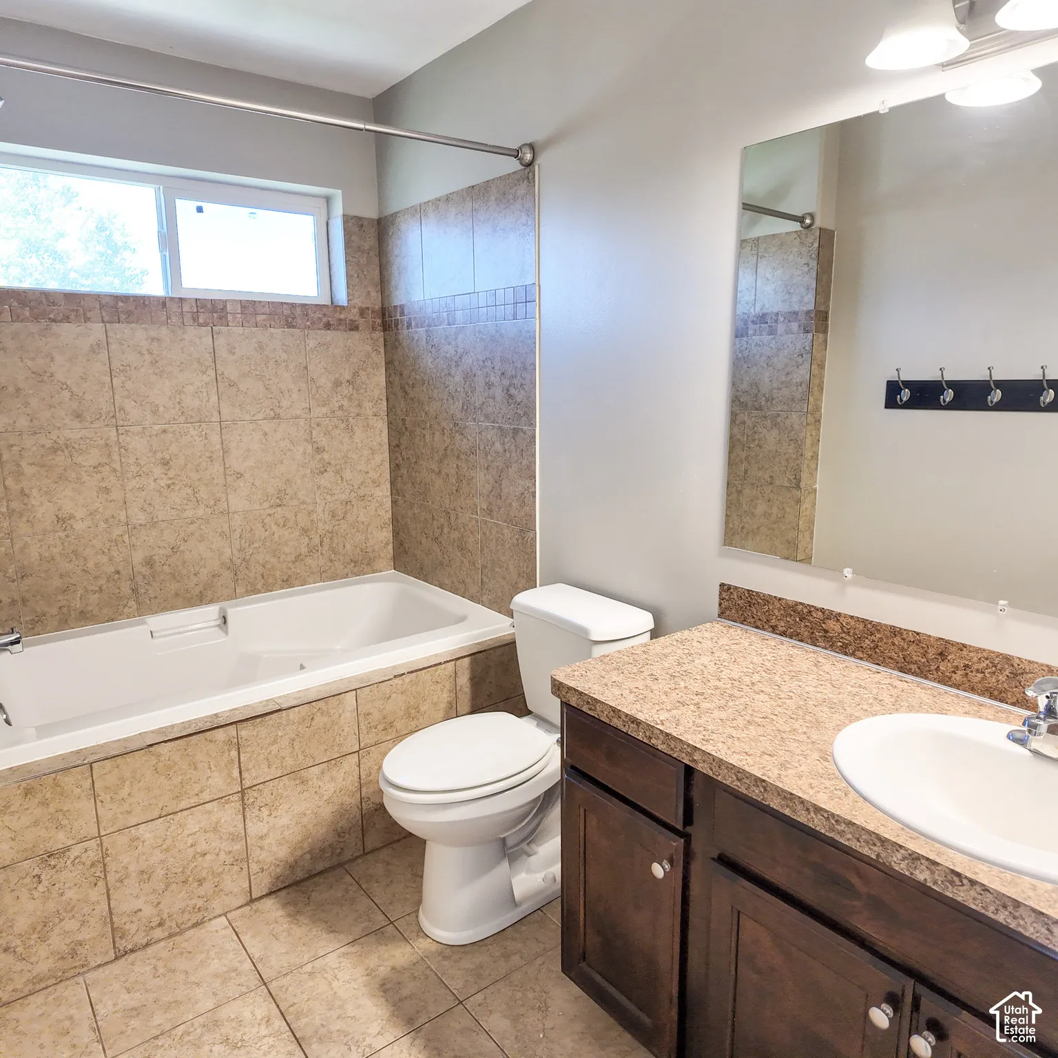 Bathroom featuring a built-in tub, tiled shower surround with accent band, vanity with integrated sink, and a large wall-mounted mirror