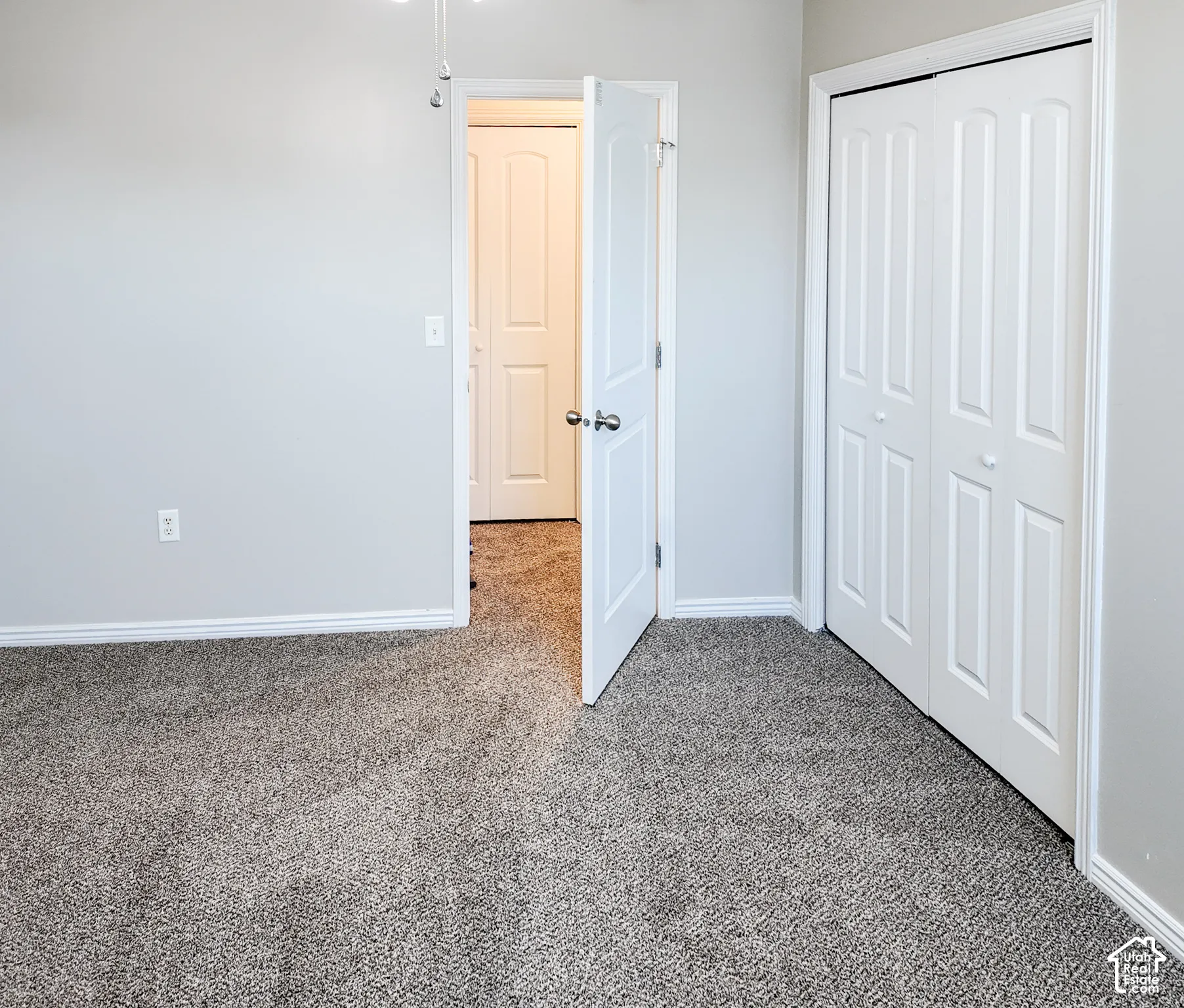 Wall-to-wall carpeting, light gray wall paint, white trim, and a white bi-fold closet door