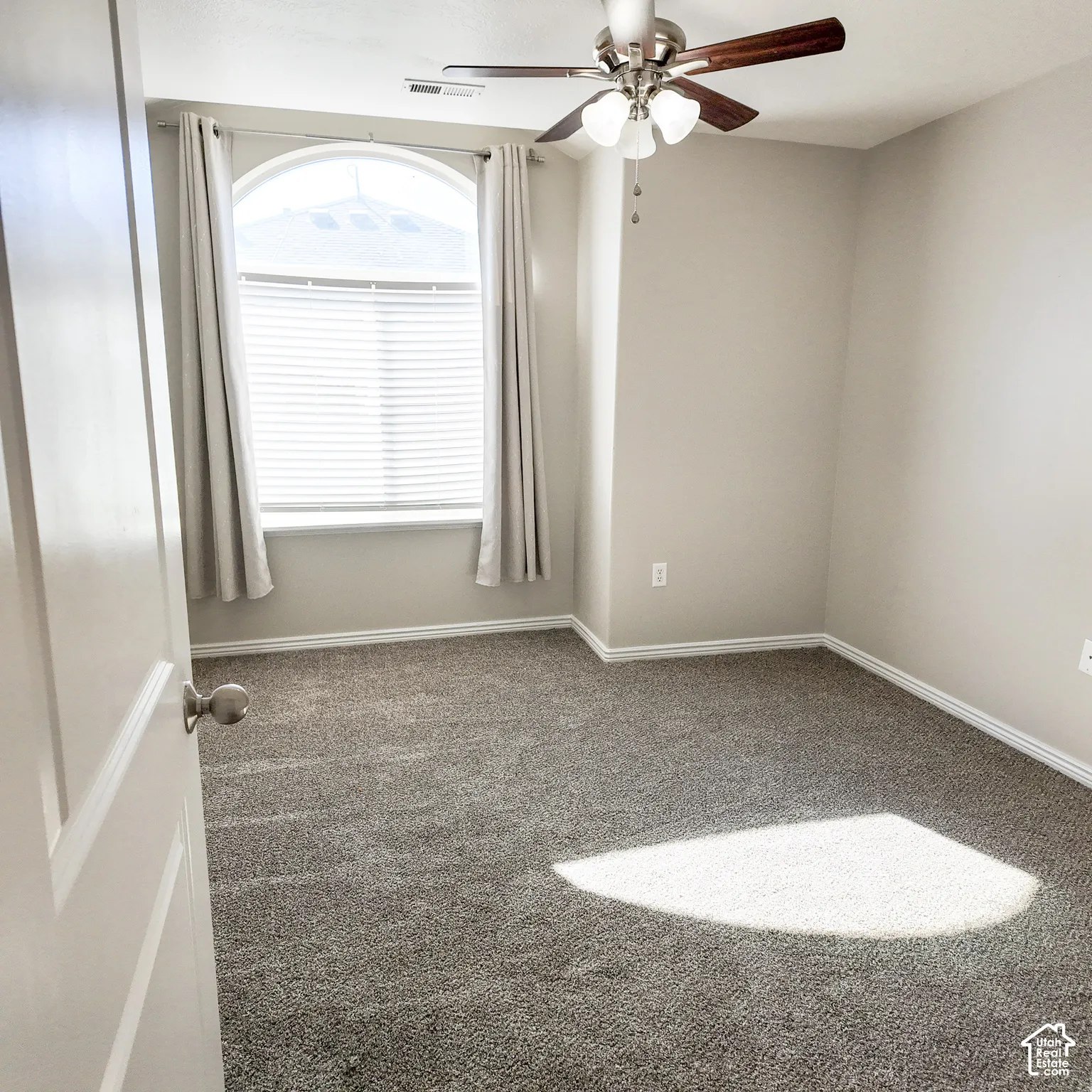 Arched window with blinds, ceiling fan with light fixture, neutral wall paint, and gray carpeting